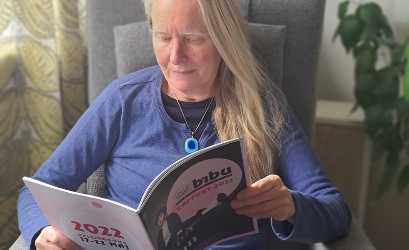 En kvinna, Irene Grahn, sitter i en fåtölj och läser bibu 2022-rapporten
