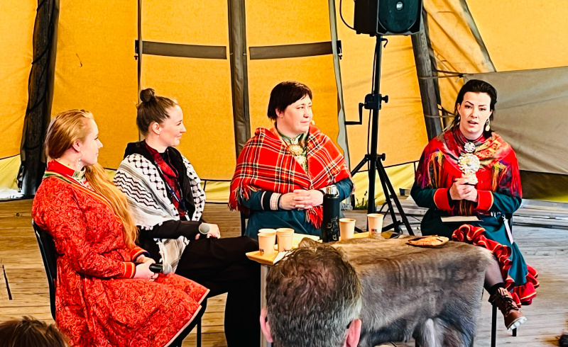 Fyra kvinnor i traditionella samiska kläder sitter och samtalar i en kåta.