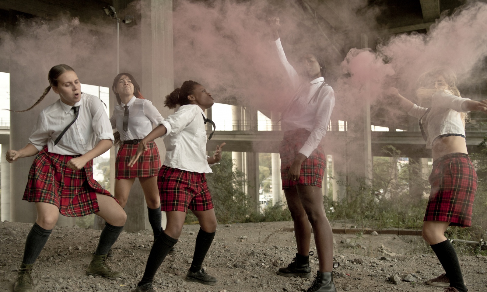 The dance group of five named "JUCK" . Four of them are dancing, and one is raising a fist in the air in a cloud of pink smoke. 