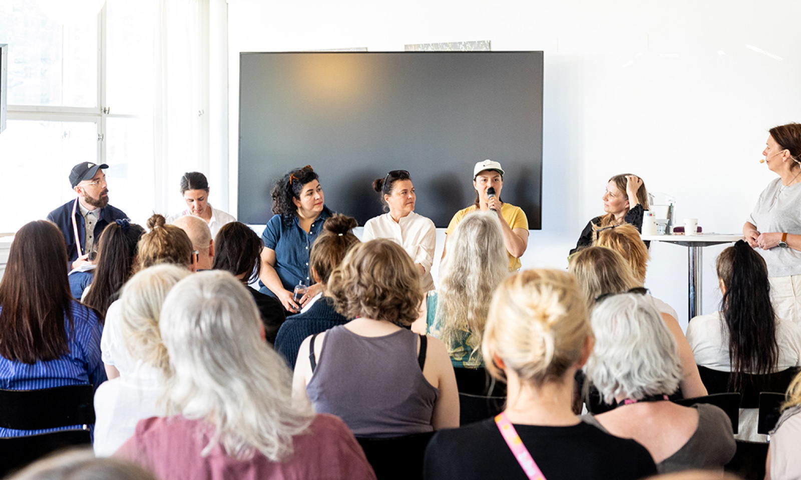 Flera personer sitter uppradade för att hålla ett seminarie. Vi ser några huvud i publiken bakifrån.