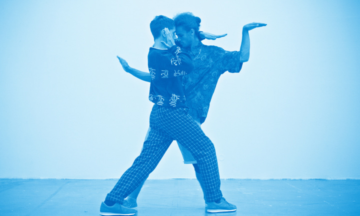 Två personer dansar uttrycksfullt nära varandra med ingenting utom en ljus vägg i bakgrunden. Hela bilden är tintad med ett blått skimmer.