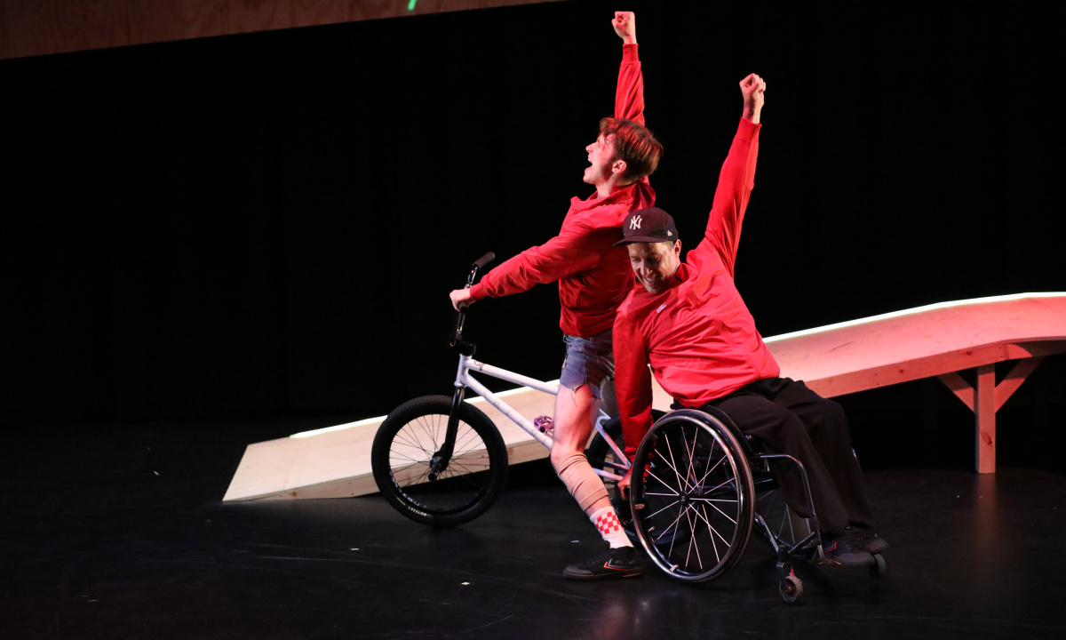 Två dansare i röda tröjor varav en använder en rullstol