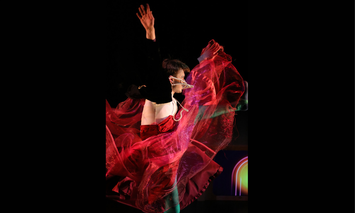 En man i röd tullkjol sträcker upp armarna i en häftig rörelse