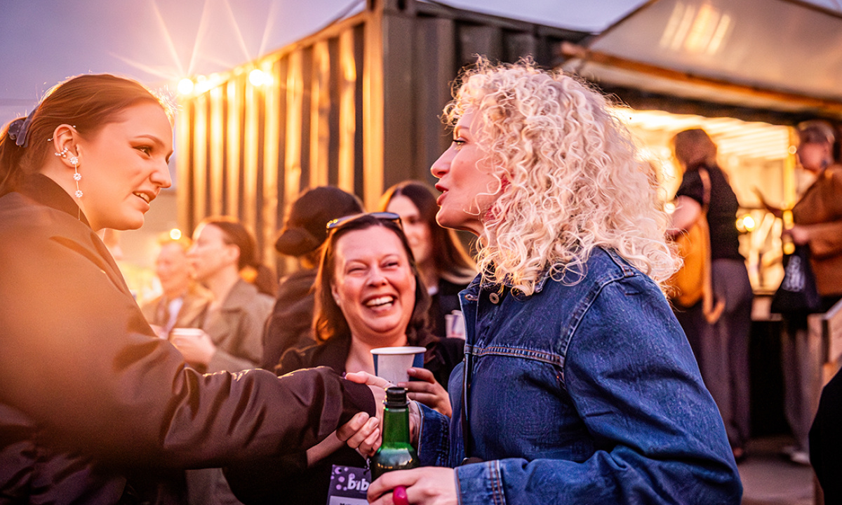 Kvinna med ljust lockigt hår pratar med andra på fest