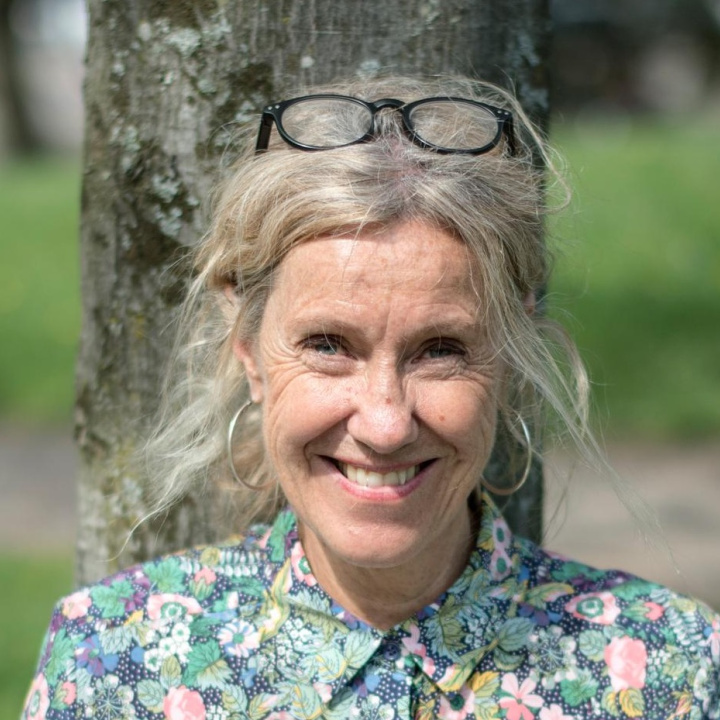 Ljushyad kvinna i övre medelålderna med ljust lockigt uppsatt hår, leende läppar och blommig skjorta