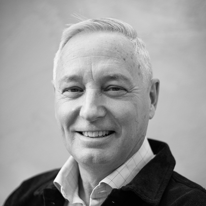 Smiling upper-middle-aged man with fair skin and short hair wearing a shirt and a black jacket.