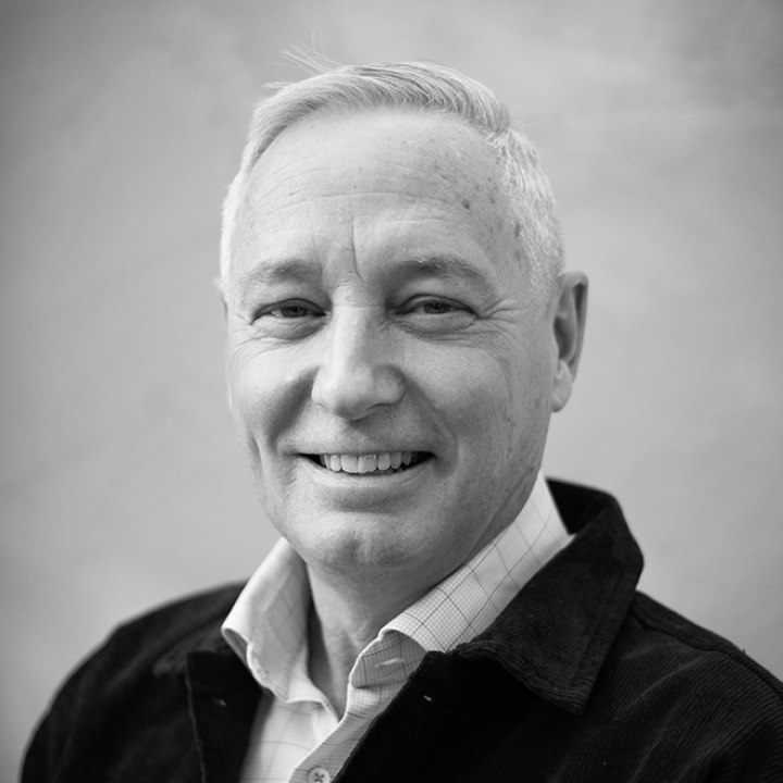 Smiling upper-middle-aged man with fair skin and short hair wearing a shirt and a black jacket.